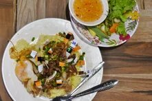 A plate of grilled pork and rice, a typical Cambodian breakfast, with pieces of a credit card sprinkled on it to illustrate the presence of microplastics in the food we consume. 